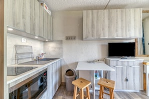 Moderni keittiö, jossa on sisäänrakennettu uuni, pesuallas, televisio ja puiset jakkarat.