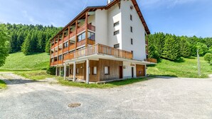 A two-story building with a wooden balcony, a covered entrance, and a view of a forested hillside. - Well-Equipped Studio with Enclosed Balcony and Mountain View (La Morte)