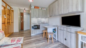 A compact kitchen with a built-in oven, a small dining area with stools, a TV mounted on the wall, and wooden cabinets. - Well-Equipped Studio with Enclosed Balcony and Mountain View (La Morte)