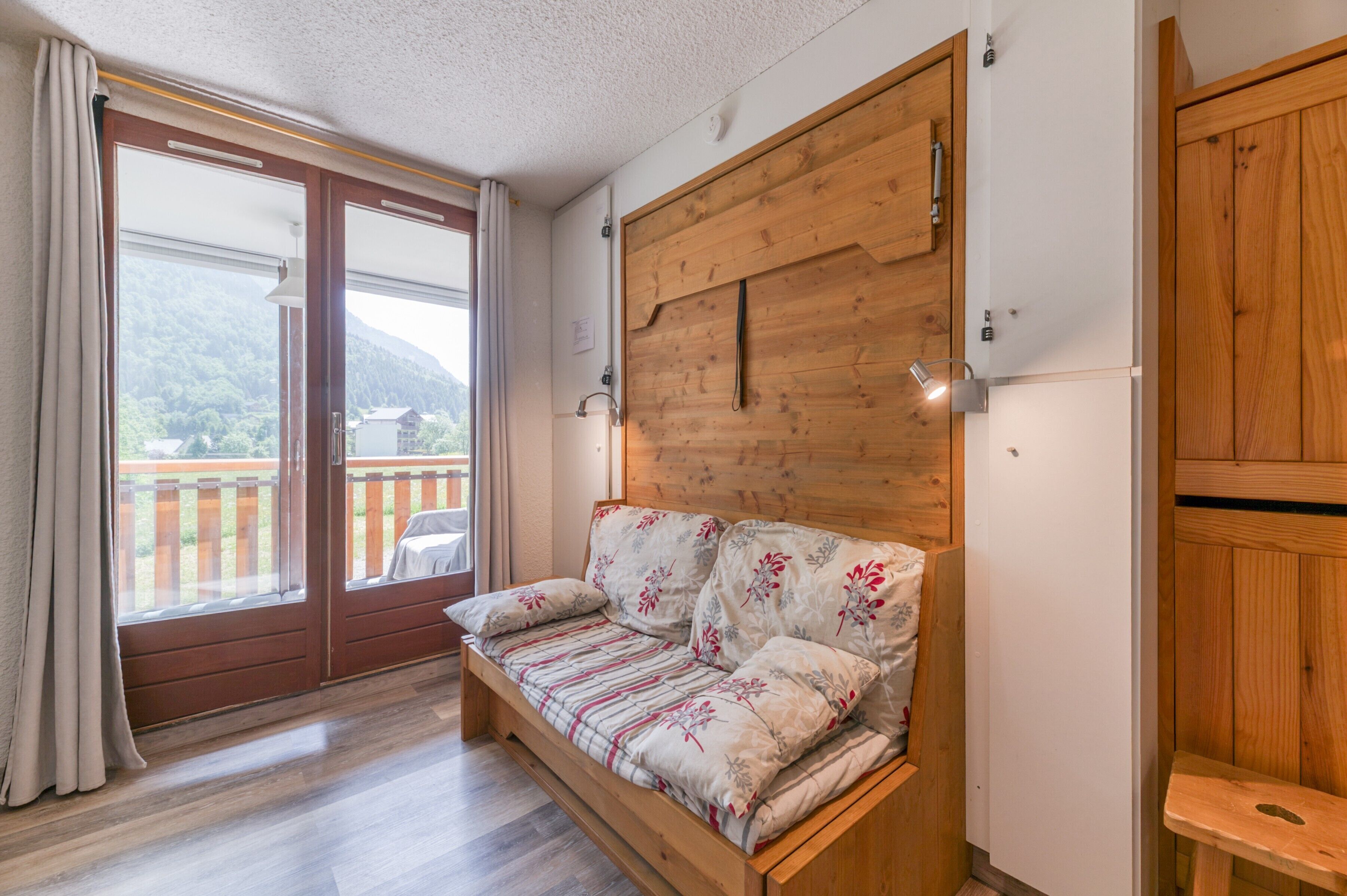 Ein Zimmer mit einer Holzcouch, einer Schiebetür zum Balkon und einem Holzkabinett.
