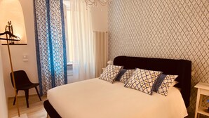 Une chambre à coucher avec un grand lit, une chaise, une table de chevet, un lustre et des rideaux à motifs.
