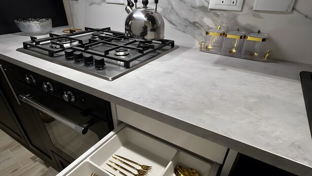 Une cuisine moderne équipée d’une cuisinière à gaz, d’une bouilloire et d’un tiroir contenant des ustensiles dorés.