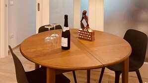 Une table ronde en bois, avec une bouteille de vin, deux verres à vin, une figurine décorative en bois et une lampe de sol moderne.