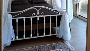 A four-poster bed with white curtains, a floral wallpaper, and a framed picture on the wall.