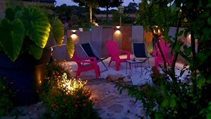 An outdoor seating area with chairs and tables, surrounded by plants and a stone wall.