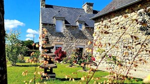 A stone house with a grassy yard, a stone wall, and a clear blue sky.