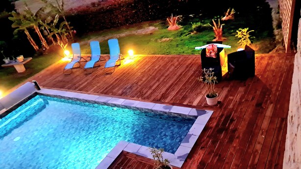 A swimming pool with a wooden deck, lounge chairs, and potted plants.