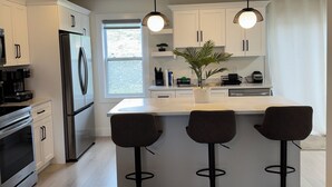 Una cocina moderna con armarios blancos, un refrigerador de acero inoxidable, horno empotrado y una barra con tres taburetes.