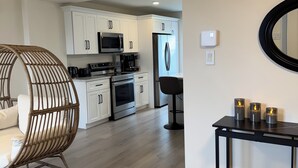 Una cocina moderna con armarios blancos, electrodomésticos de acero inoxidable y una zona de comedor con una silla y una mesa de mimbre.