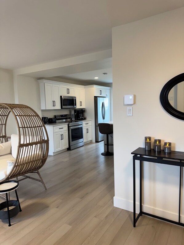 Una cocina moderna con armarios blancos, electrodomésticos de acero inoxidable y una zona de comedor con una silla y una mesa de mimbre.