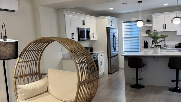 Una cocina moderna con armarios blancos, electrodomésticos de acero inoxidable y una silla redonda de mimbre con asiento acolchado.