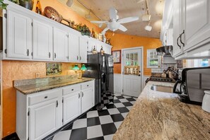 Une cuisine avec des meubles blancs, un sol à carreaux noirs et blancs, un ventilateur de plafond et une lampe verte.