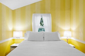 A room with yellow walls, a bed with white bedding, two bedside tables with lamps, and a window with white curtains. - Beach Pass Included! (Barnstable)