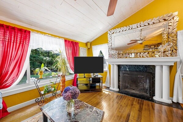 A room with a fireplace, a television, and a view of greenery outside. - Beach Pass Included! (Barnstable)
