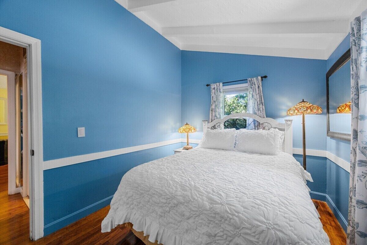 Un dormitorio con una cama grande, dos lámparas de noche, una ventana con cortinas y un espejo en la pared.