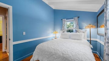 Un dormitorio con una cama grande, dos lámparas de noche, una ventana con cortinas y un espejo en la pared.