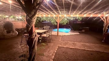 Um pátio externo com piscina, área de estar coberta e pérgola com luzes de cordão.