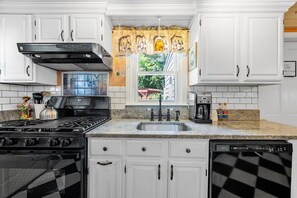 A kitchen with white cabinets, a black stove, a sink, and a window with a view of greenery. - Beach Pass Included! (Barnstable)