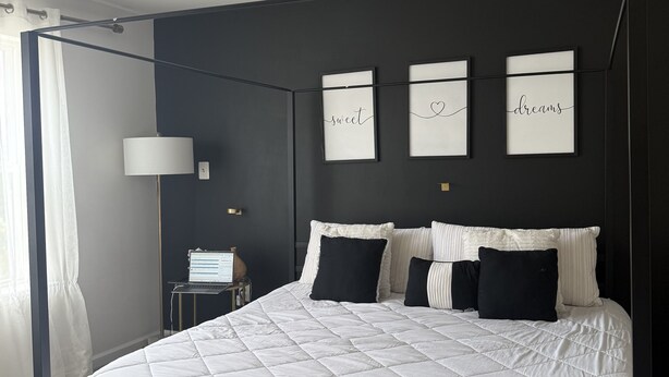 Ein modernes Schlafzimmer mit schwarzem Kopfteil, weißer, gesteppter Bettdecke und drei gerahmten Motivationssprüchen an der Wand.