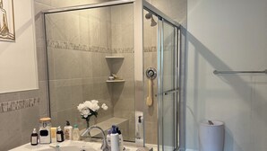 Ein modernes Badezimmer mit einer Duschkabine, einer großzügigen Badewanne und einem Waschtisch mit Pflegeprodukten.