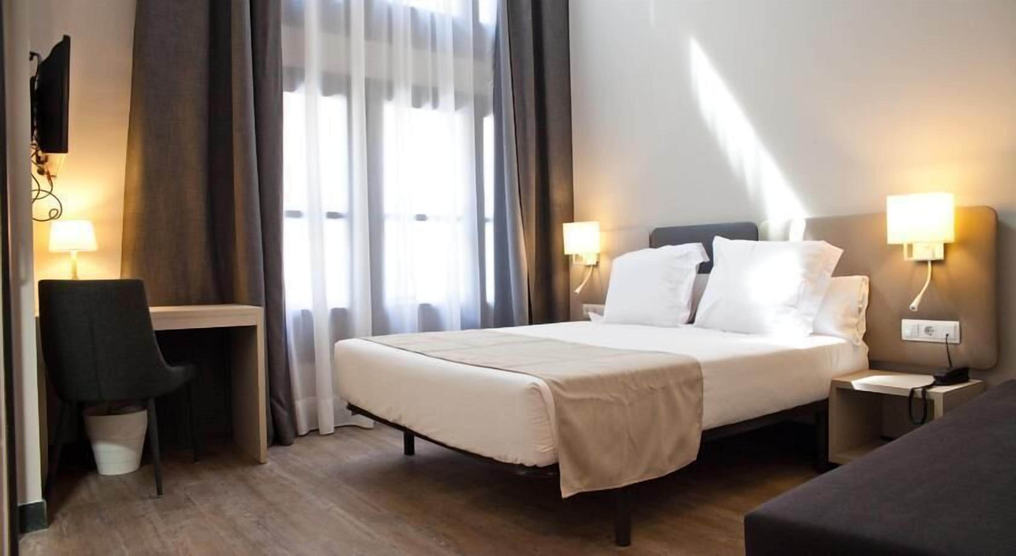 A hotel room with a bed, bedside tables, a desk, and a chair.