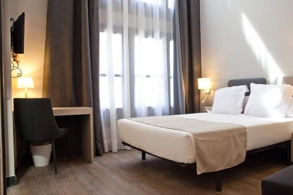 A hotel room with a bed, bedside tables, a desk, and a chair.
