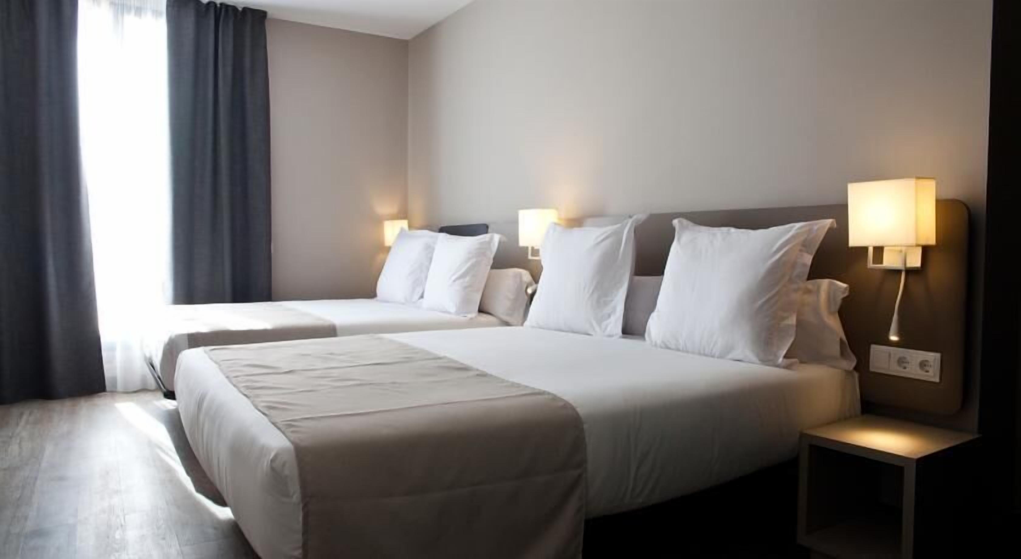 A hotel room with two beds, a nightstand, and a lamp.