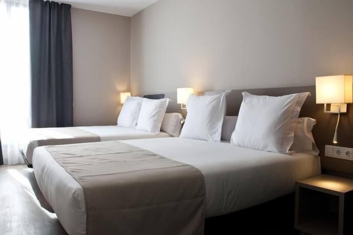 A hotel room with two beds, a nightstand, and a lamp.