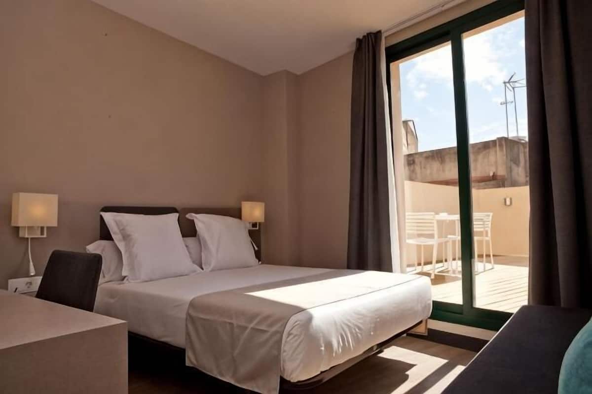 A hotel room with a bed, two bedside lamps, a desk, and a view of an outdoor patio with chairs.