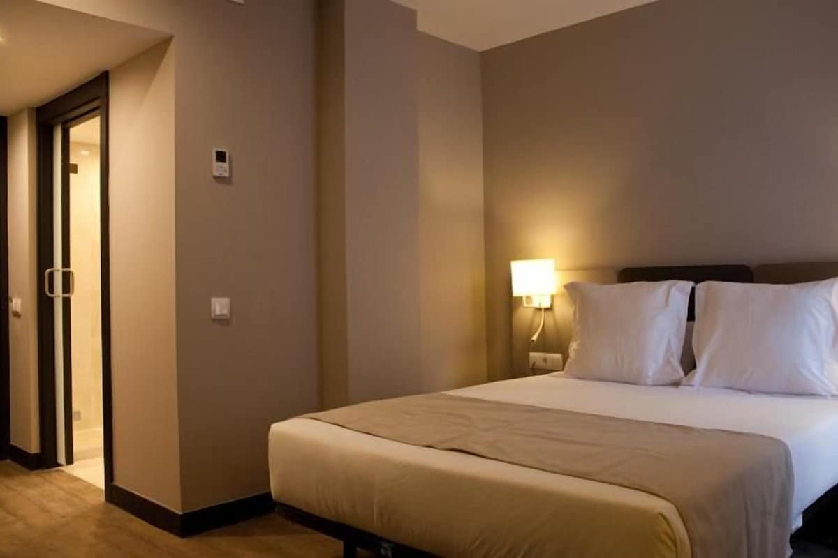 Una habitación de hotel con una cama grande, dos lámparas de noche y una puerta que da a otra habitación.