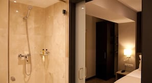 A modern bathroom with a glass-enclosed shower, a vanity with a mirror, and a bedside table with a lamp. - May Ramblas Hotel (Barcelona)