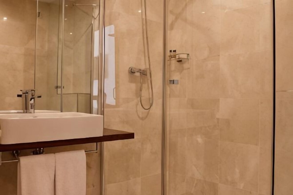 A modern bathroom with a glass shower enclosure, a sink with a mirror, and a towel rack.
