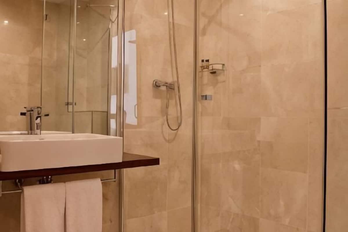 A modern bathroom with a glass shower enclosure, a sink with a mirror, and a towel rack.