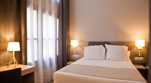 A hotel room with a large bed, two bedside tables, and two wall-mounted lamps.