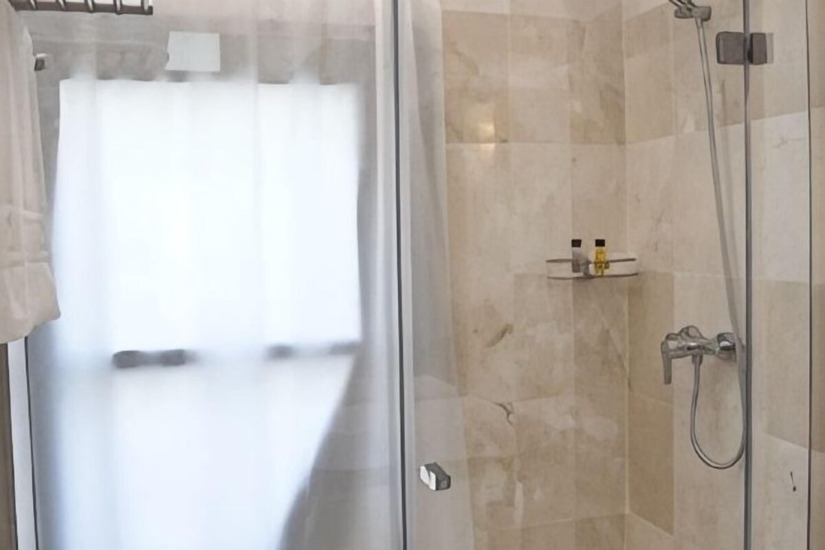 A glass-enclosed shower area with a tiled wall, a shelf with toiletries, and a visible bathroom door.