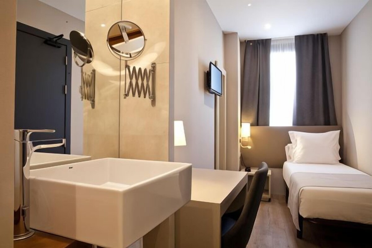 A modern hotel room with a large bathtub, a bed, a TV, and a window with curtains.