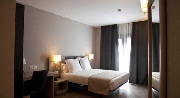 Una habitación de hotel con cama, lámparas de noche, escritorio y una silla.