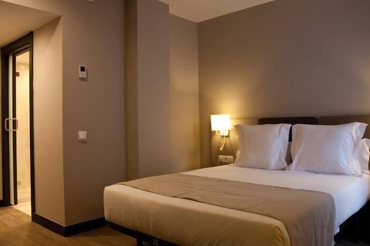 A hotel room with a bed, two bedside lamps, a nightstand, and a door.