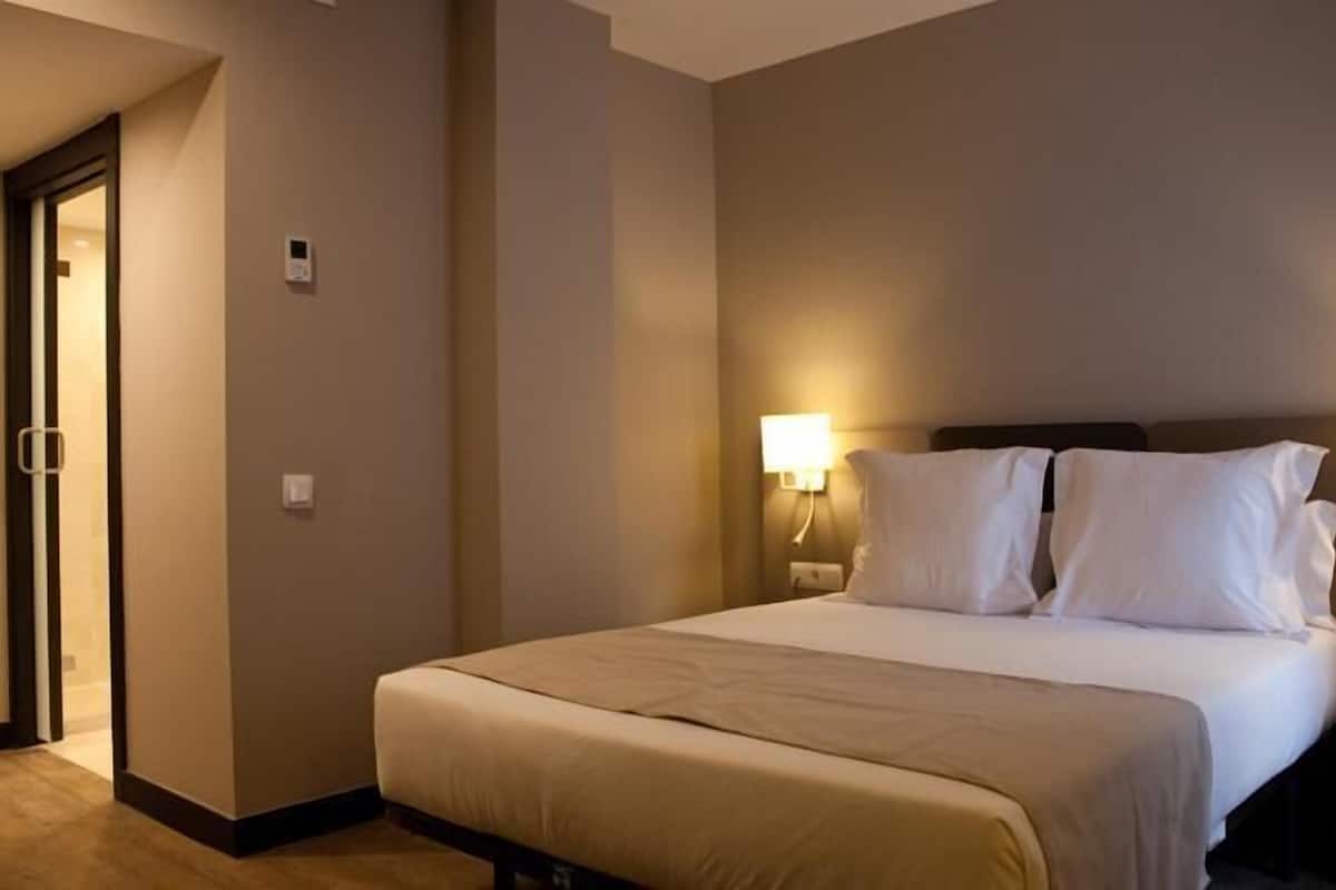 A hotel room with a bed, two bedside lamps, a nightstand, and a door.