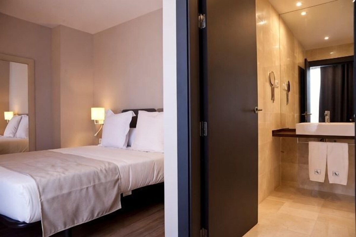 A hotel room with a bed, bedside lamps, a bathroom with a mirror, and a towel rack.