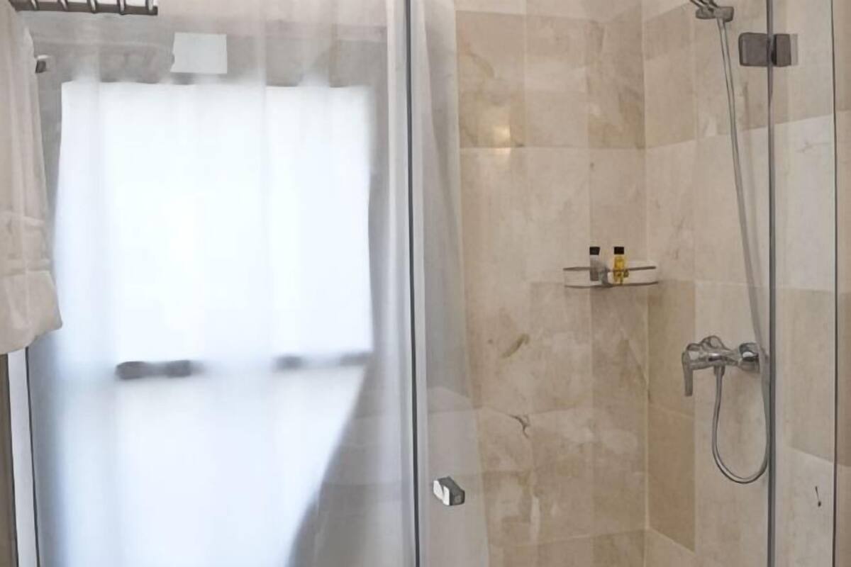 A glass-enclosed shower area with a tiled wall, a shelf with toiletries, and a visible bathroom door.