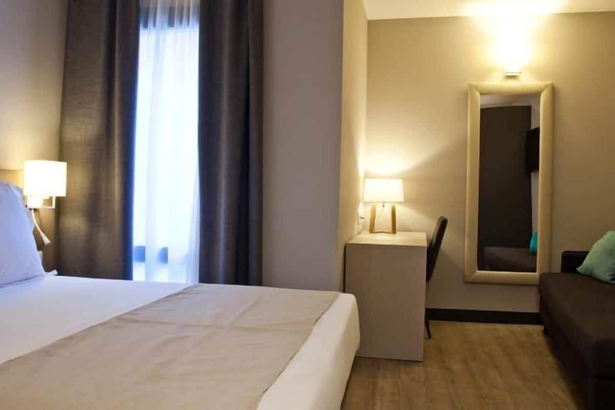 Una habitación de hotel con una cama, un escritorio, una silla y un sofá.