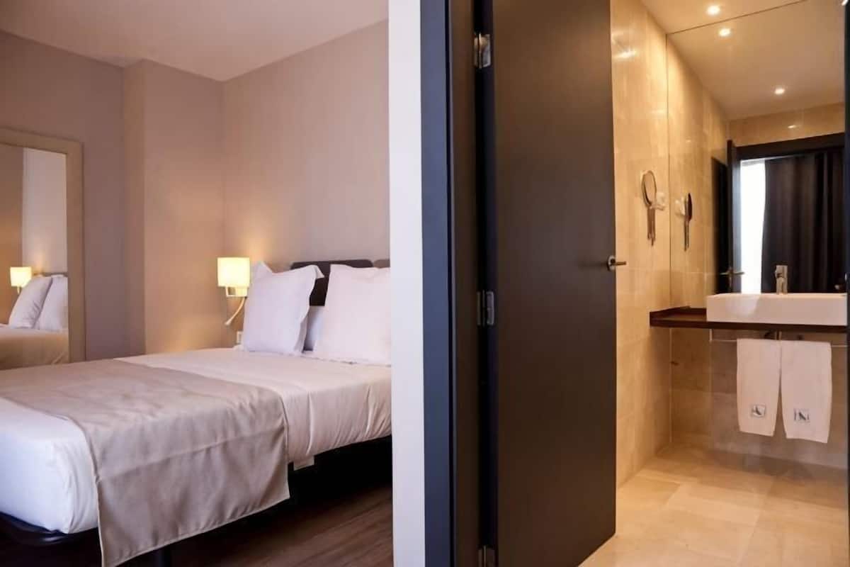 A hotel room with a bed, bedside lamps, a bathroom with a mirror, and a towel rack.