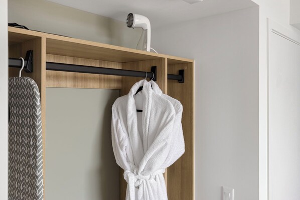 Ein Badezimmer mit einem Holzboden, einem weißen Bademantel, der an einem Haken hängt, und einem Föhn auf dem Boden.