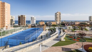 A sports court with a blue surface, surrounded by a stone wall and a metal fence.