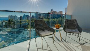 A balcony with two wicker chairs, a small table with fruit, and a city view.