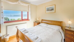 A bedroom with a wooden bed, a view of a lake, a radiator, a wicker basket, and a nightstand with a lamp.