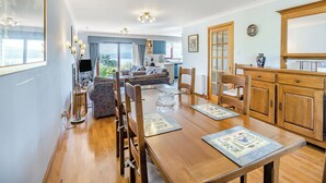 A spacious living area with a wooden dining table, comfortable seating, a kitchen area, and a large window offering a view.
