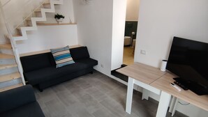 Ett modernt vardagsrum med en trappa, en svart soffa, ett träbord och en tv.