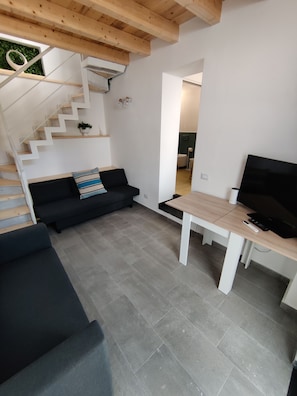A modern living room with a staircase, a black sofa, a wooden table, and a TV.